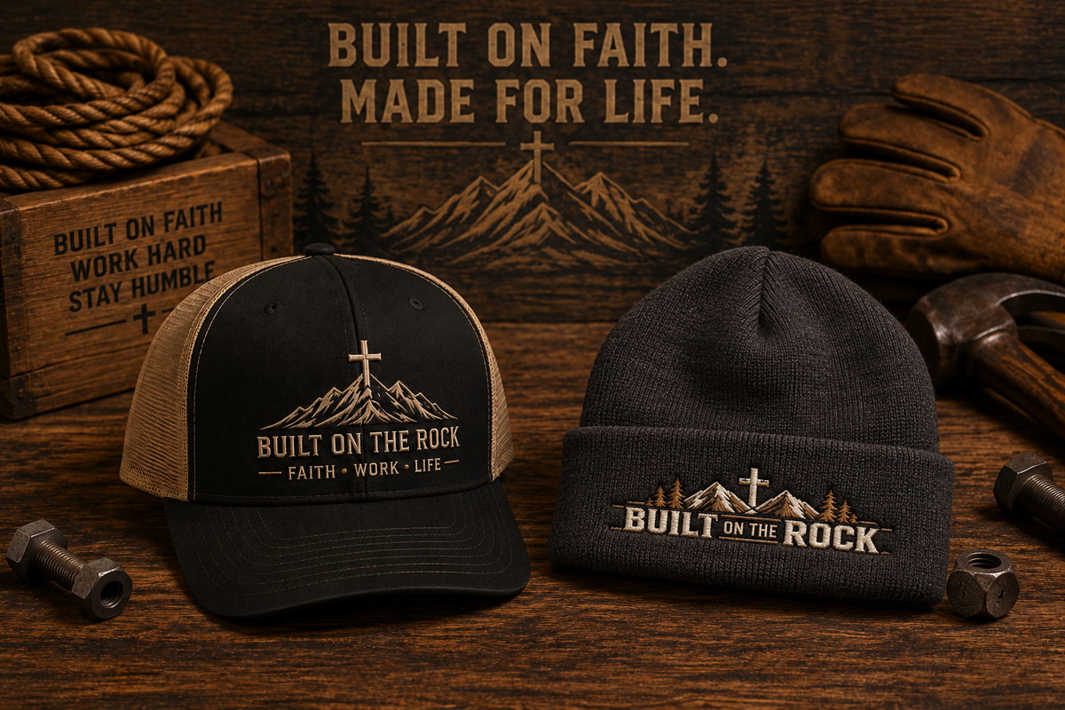 Built on the Rock trucker cap and dark gray embroidered beanie on a rustic wooden workbench.